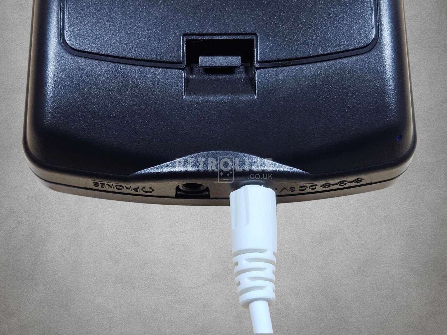 Close-up of a black game boy color with a blue light on a grey background