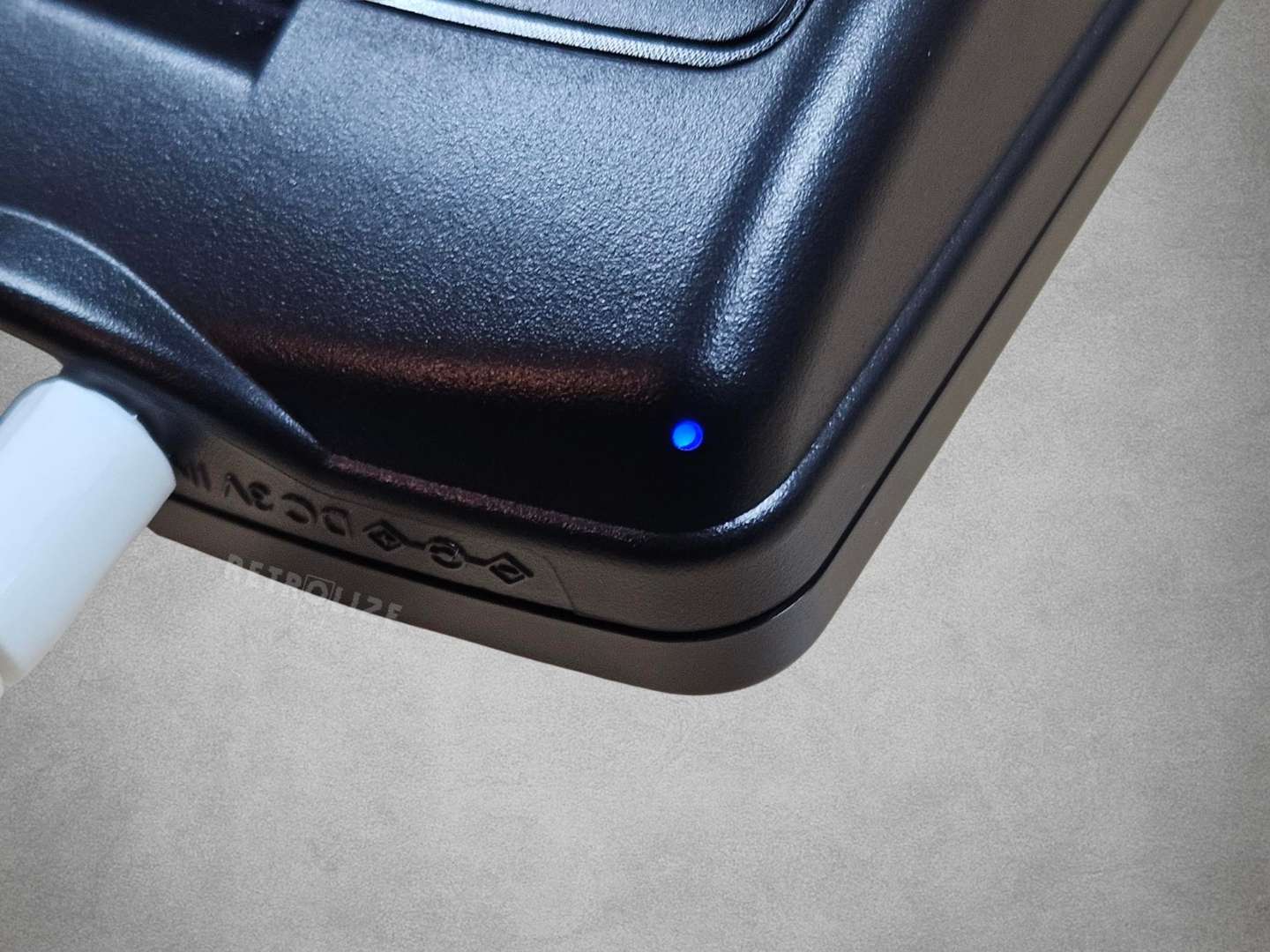 Close-up of a Game Boy Color with a blue charging light on a grey surface

