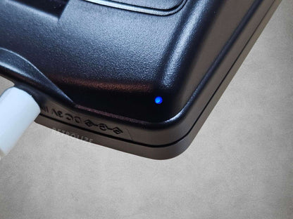 Close-up of a Game Boy Color with a blue charging light on a grey surface
