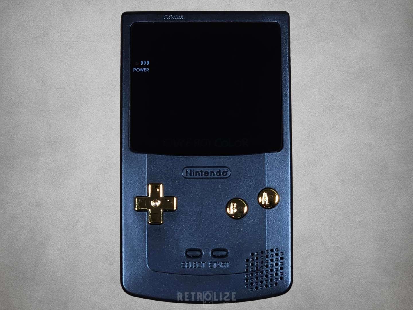 Black Nintendo Game Boy with gold buttons on a grey background

